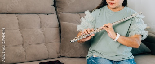 Canvas Print A flutist in a green top sits comfortably on a gray sofa, preparing her silver flute