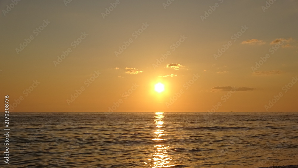 Fototapeta premium Glowing Bright Sun and Golden Horizon Over Calm Ocean at Sunrise. A breathtaking view of the bright sun rising over the calm ocean horizon, creating a brilliant golden path of sunlight.