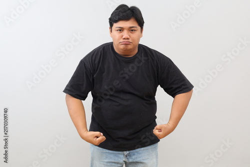 Obraz na plátne A burly, muscular male athlete stands against a white background, showing off his somewhat heavy-set physique and arm muscles while striking a tough-guy pose