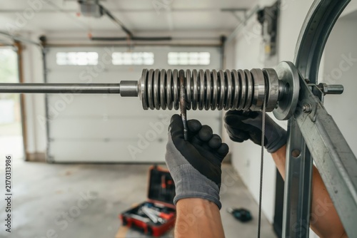 Professional technician adjusting a garage door torsion spring with winding bars in a residential garage setting