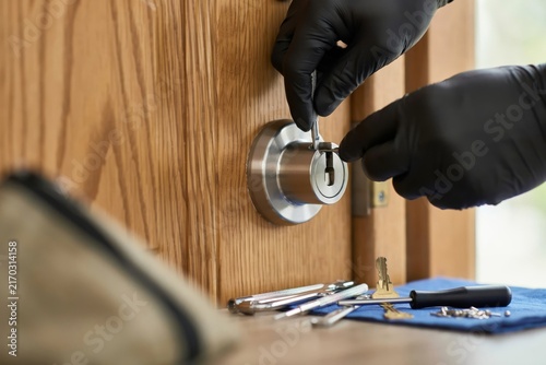 Locksmith using professional tools to pick a door lock, closeup of hands in black gloves working on a wooden door mechanism