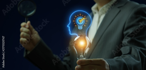 Close-up vertical shot of hand holding magnifying glass to inspect glowing lightbulb in human head profile thinking idea. Cognitive thought process analysis, intellect innovation, and wisdom concept.