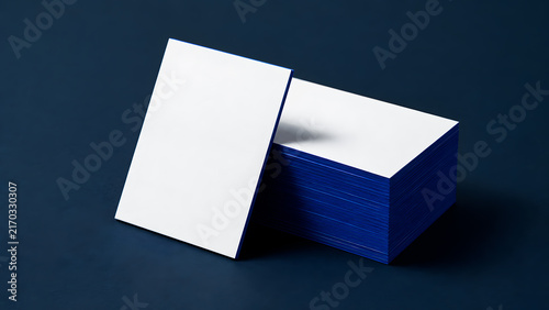 Stack of blank white business cards with deep blue edges leaning on a dark blue background. Corporate identity mockup, professional stationery branding concept with copy space