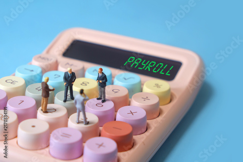 Miniature businessmen standing on calculator discussing employee salary with PAYROLL text on screen