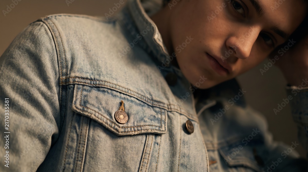 Obraz premium denim jacket worn by young man leaning close in soft warm light portrait