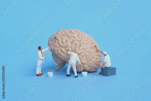Miniature figures of maintenance workers cleaning and caring for a human brain model on blue background, concept of mental health care, brain maintenance, and neurology study.