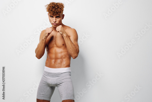 Принти на полотні Young athletic man with muscular body posing in fighting stance wearing gray shorts against white background