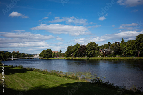 Fotografie River Ness in Inverness with suspension bridge, trees and buildings under blue s
