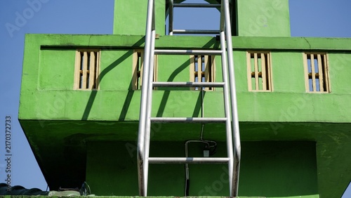 Frontal symmetry of a metal access ladder leading up a bright green Islamic mosque tower structure.