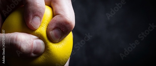 Hand squeezing bright yellow stress ball tightly to relieve tension and anxiety in a dark setting.