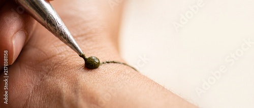 Detailed application of dark green henna paste onto skin using metal cone tool for traditional decorative body art celebration.