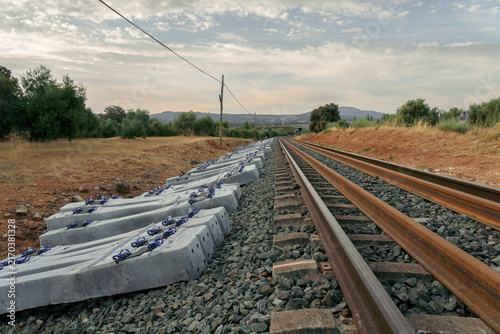 New railway construction project with fresh concrete sleepers stacked next to existing tracks, showing infrastructure development under a cloudy sky