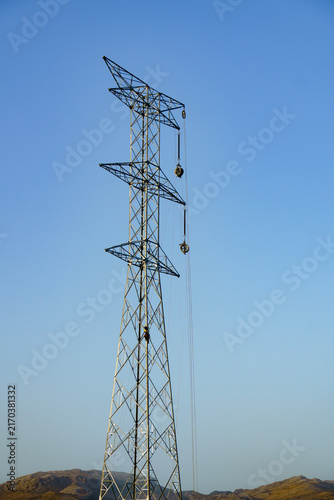 Electrical worker on a steel lattice transmission tower, installing new high voltage power lines across a clear sky
