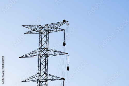 Lineman working at height on an electricity pylon, installing equipment for high voltage power transmission lines against a clear sky