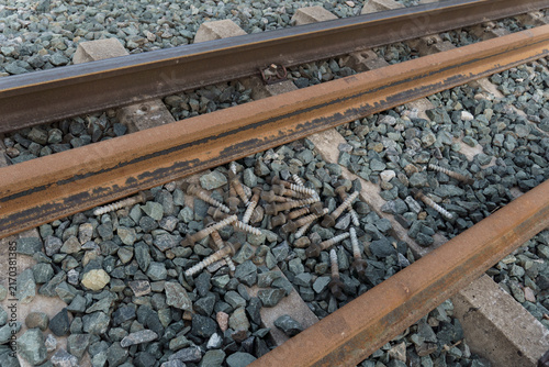 Railway tracks showing rust and a pile of discarded metal screws on the gravel ballast, depicting construction or repair