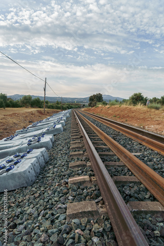 New railway construction project with fresh concrete sleepers stacked next to existing tracks, showing infrastructure development under a cloudy sky