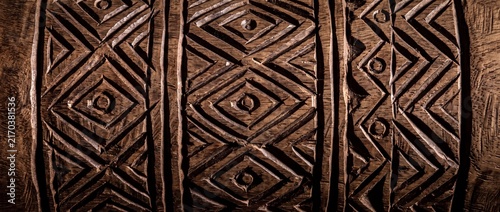 Traditional african tribal wood carving with geometric diamond patterns and circular symbols exhibits ancient cultural heritage.