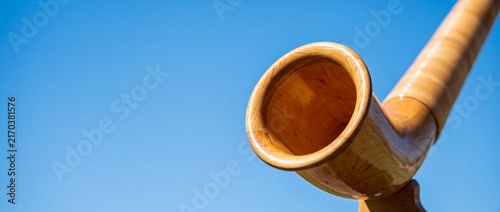 Wooden alphorn bell opening against clear blue sky in swiss alps signifies traditional mountain music and cultural celebration.