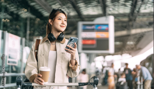 Young adult asian woman with travel luggage using smartphone app call taxi service transfer at international airport shuttle bus terminal