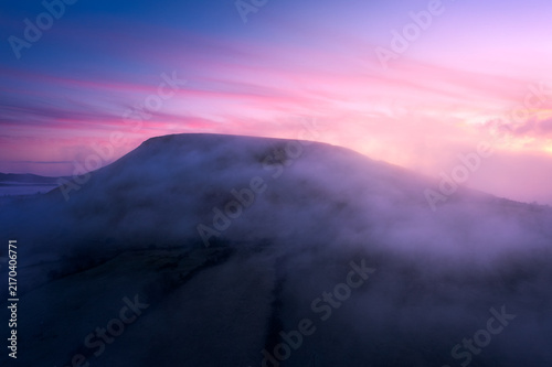 Aerial view of a mountain shrouded in thick morning mist under a vibrant pink and purple sky at sunrise in Sligo, County Sligo, Ireland.