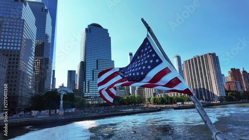American flag waves on boat creating wake, revealing New York City skyline on sunny day