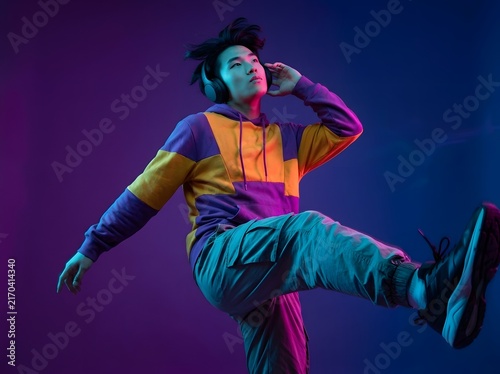 Young man in hoodie dancing with headphones under neon light