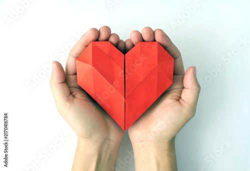 Hands gently holding a red origami heart symbolizing love and creativity in crafting