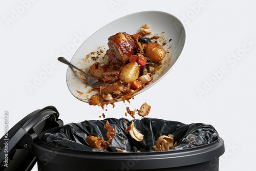Discarded plate of food being thrown into a kitchen trash can  