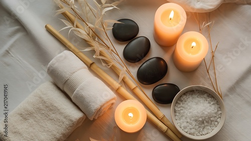 Spa treatment accessories featuring black massage stones white towels bamboo stalks and warm glowing pillar candles