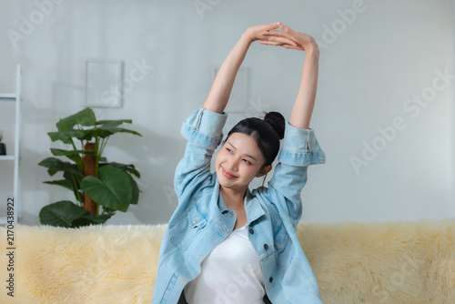 фотографія smiling woman stretching her arms while relaxing on sofa at home, enjoying calm morning and healthy lifestyle, wellness, stretching, relaxation, health
