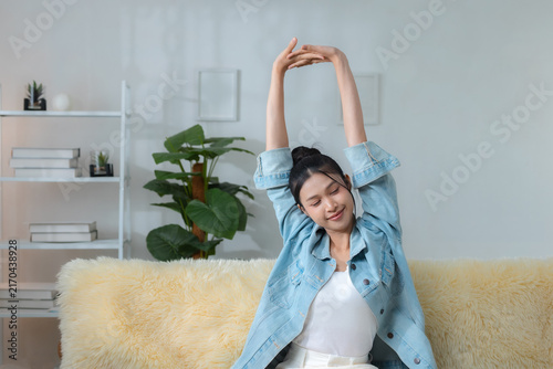 Картината върху платно smiling woman stretching her arms while relaxing on sofa at home, enjoying calm morning and healthy lifestyle, wellness, stretching, relaxation, health
