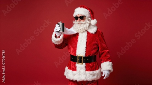 Modern Santa Claus in red suit holding metal flask against red background