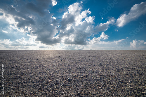 Konstfotografi Vast gravel plain under dramatic blue sky with white clouds and sunlight in Xinj