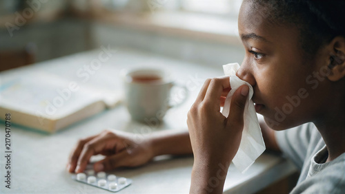 Seasonal colds and immune system support, close-up portrait of a black American teenage girl sitting at a table, with a blister pack of pills and a mug of hot tea nearby, copy space for text