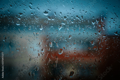 Obraz na płótnie Close-up of water droplets on a glass window with a blurred urban background, sh