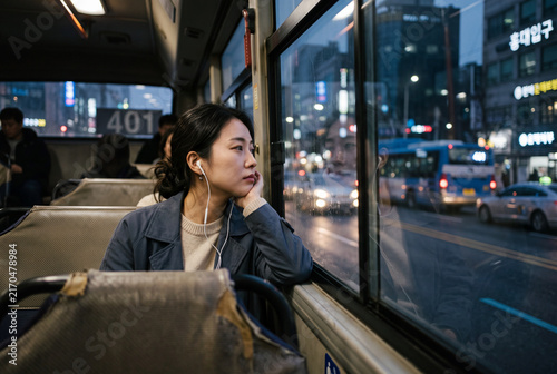 Woman sitting on city bus looking out window at night traffic for urban commute background and contemplative lifestyle scene