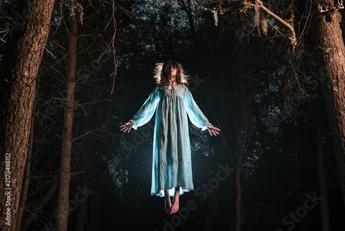 Eerie girl levitates in dark forest at night, embodying Halloween spirit