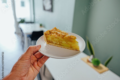 Cuadro en lienzo Hand holds a white plate with a golden apple tart slice topped with toasted almo