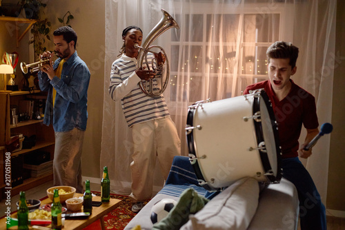 Obraz na płótnie Diverse young adult male football fans playing musical instruments at home celebrating victory