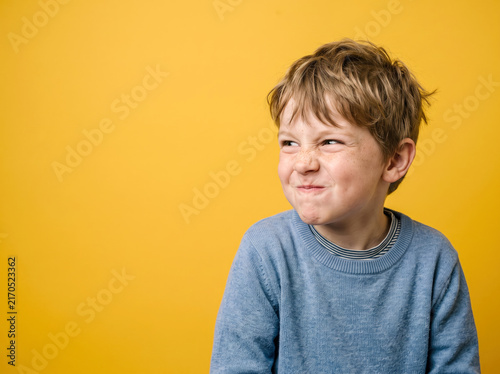Boy making funny face with a wrinkled nose against a bright yellow background