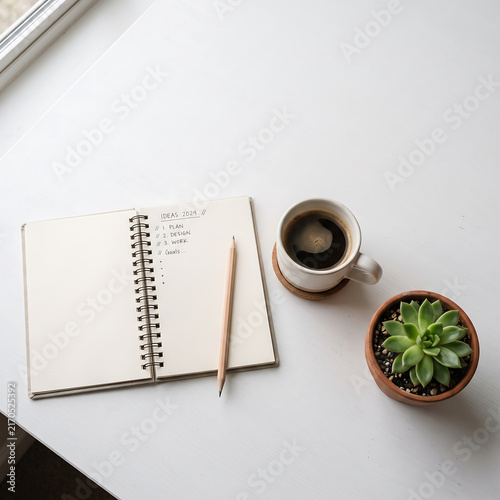 A clean white desk with a to-do list notebook, pencil, coffee cup, and succulent plant bathed in soft morning light.