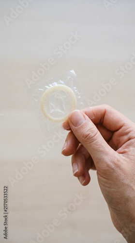 Female hand holding a condom wrapper in a neutral setting  