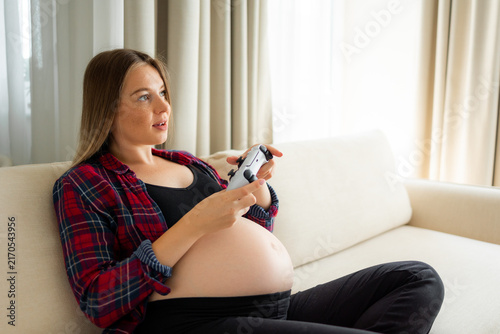 Cuadro en lienzo Pregnant woman playing video games on a couch, relaxed and expectant in casual h