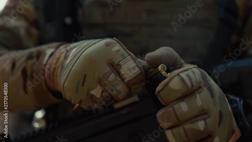Extreme close-up of soldier's hands in camouflage tactical gloves manually loading ammunition bullets into rifle magazine one by one in combat environment. Military warfare concept for defense, armed 