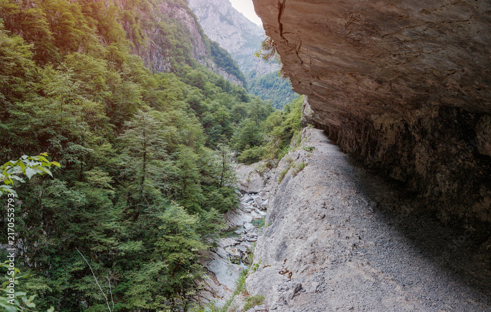 Fototapeta premium Narrow hiking path following the towering cliffs and lush forests of a dramatic Balkan gorge with a river below