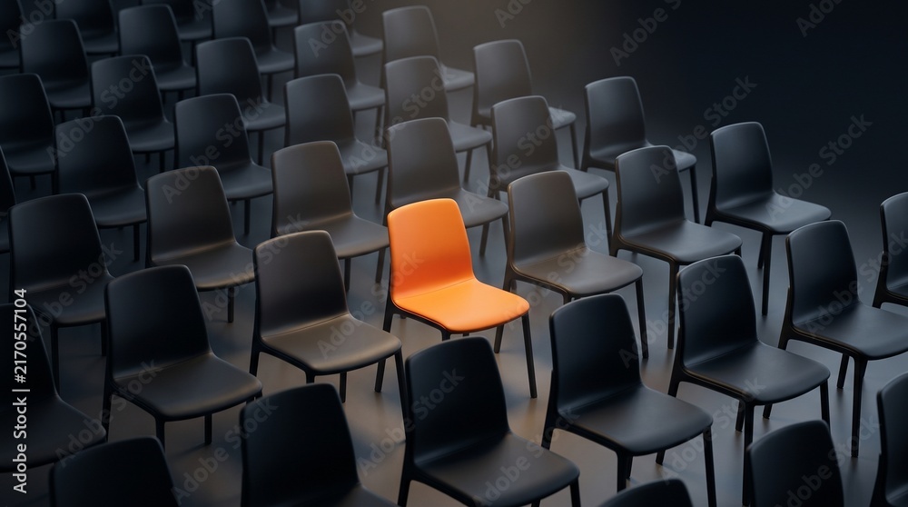 Obraz premium One bright orange chair breaking symmetry among rows of black chairs in empty auditorium