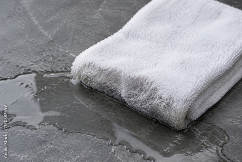 White cotton towel absorbing water from puddle on grey slate, wet and dry contrast