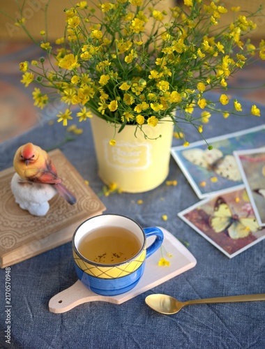 Konstfotografi A blue ceramic cup with tea and yellow wildflowers