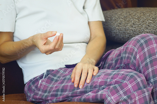 фотографія Woman sitting on couch holding single white pharmaceutical pill between fingers