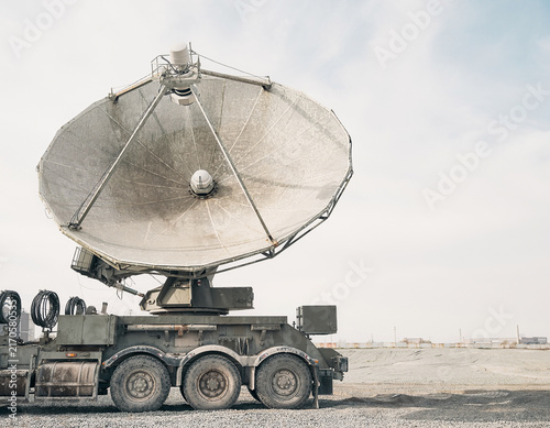 A large parabolic antenna on a heavy truck chassis, featuring a weathered matte finish and textured mesh for communications infrastructure and defense technology, with copy space.